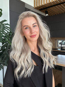 Woman wearing a thick, wavy Kim Kardashian-style wig in icy platinum with natural volume and a center part