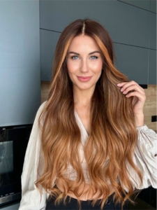 Woman wearing a long, wavy caramel brown Ariana Grande-style wig with a middle part